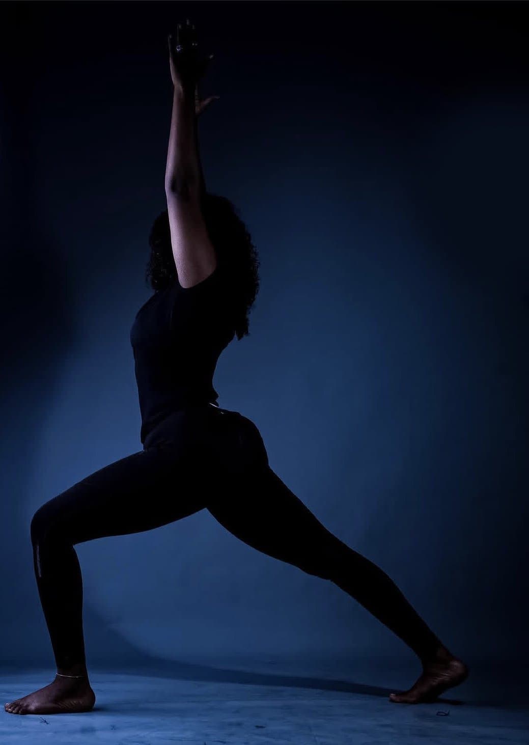Ro holding a warrior pose in a blue-lit studio